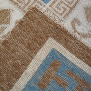 A folded rug shows cream and brown geometric patterns contrasting with a striped blue and brown border.