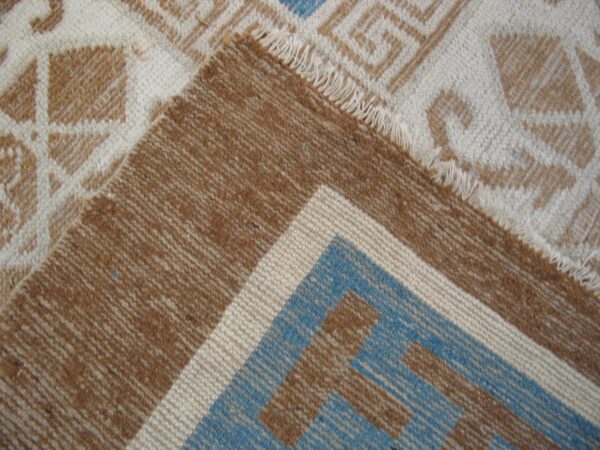 A folded rug shows cream and brown geometric patterns contrasting with a striped blue and brown border.