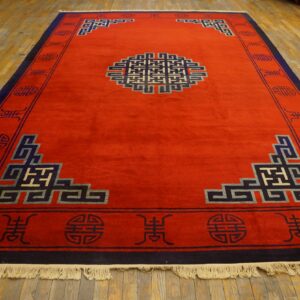 Bright red rug with a complex blue, grey, and cream geometric pattern on wood flooring.