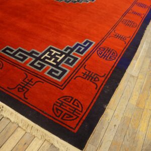 Saffron red rug featuring dark blue and black stylized symbols and knot patterns on light wood flooring.