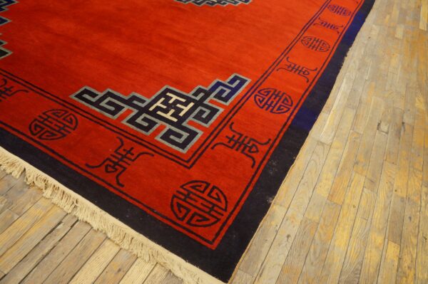 Saffron red rug featuring dark blue and black stylized symbols and knot patterns on light wood flooring.