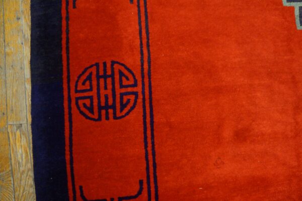 Red rug detail featuring a navy blue medallion design and border, set against light brown wooden flooring.