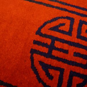 Plush red rug surface detailed with a dark blue geometric interlocking symbol.