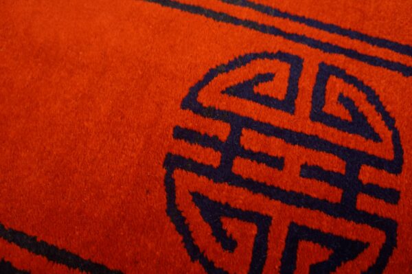 Plush red rug surface detailed with a dark blue geometric interlocking symbol.