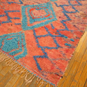 Textured salmon and bright blue rug with abstract geometric designs on wooden plank flooring.