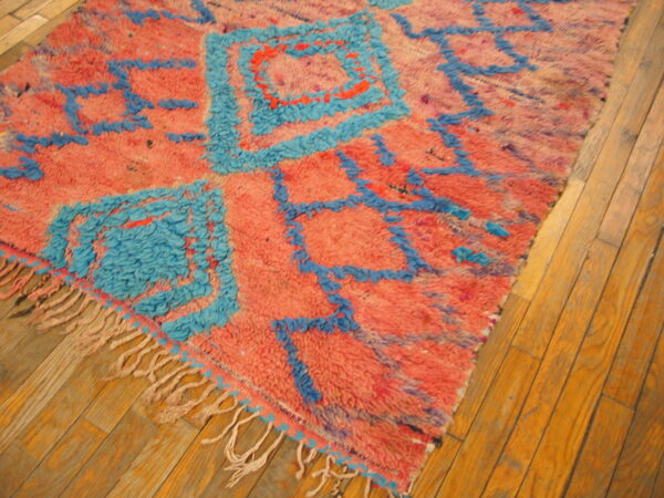 Textured salmon and bright blue rug with abstract geometric designs on wooden plank flooring.