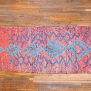 Vibrant pink high-pile rug featuring blue geometric diamonds and zigzags displayed on hardwood flooring.