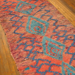 Textured coral runner rug featuring chunky turquoise geometric patterns on light brown wood flooring.