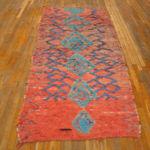 Long, textured coral rug with teal blue diamond patterns and zigzag lines on warm wood flooring.
