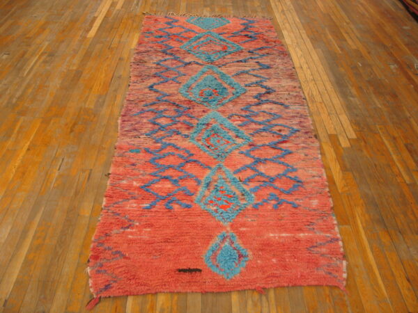Long, textured coral rug with teal blue diamond patterns and zigzag lines on warm wood flooring.