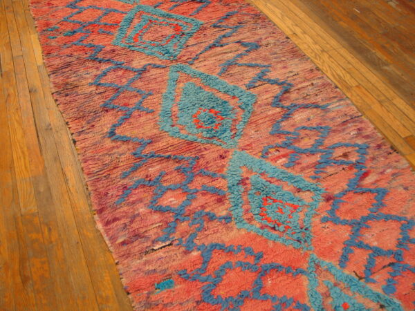 High-pile pink and turquoise rug runner featuring geometric designs on light wood flooring.
