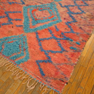 High-pile pink rug with abstract bright blue geometric designs and fringes rests on a wooden floor.