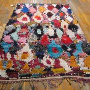 High-pile, abstract multicolor shag rug with fringe and diamond shapes on a wooden plank floor.