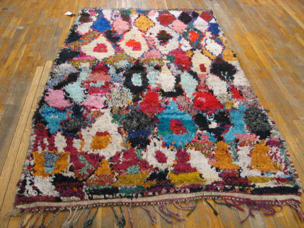 High-pile, abstract multicolor shag rug with fringe and diamond shapes on a wooden plank floor.