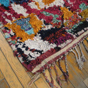 Vibrant, high-pile rag rug with braided fringe shown on light brown hardwood flooring.