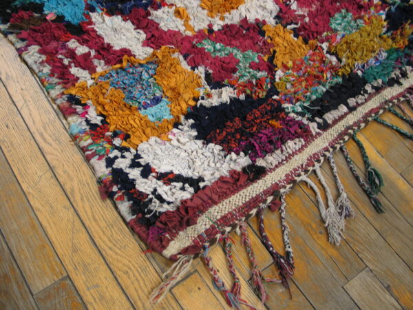 Vibrant, high-pile rag rug with braided fringe shown on light brown hardwood flooring.