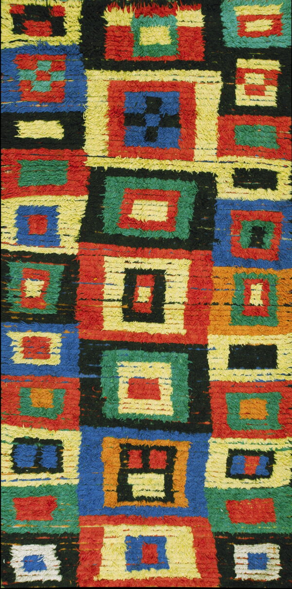 Textured, high-pile rug detail showing geometric blocks of red, blue, green, yellow, orange, and black.