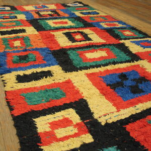 High-pile shaggy rug featuring red, blue, yellow, black, and green geometric squares on hardwood flooring.