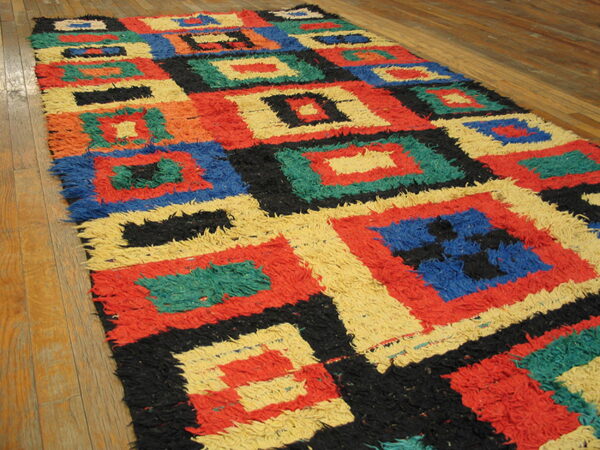 High-pile shaggy rug featuring red, blue, yellow, black, and green geometric squares on hardwood flooring.