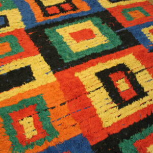 High-pile rug with nested geometric squares in red, yellow, blue, green, black, and orange on wood flooring.