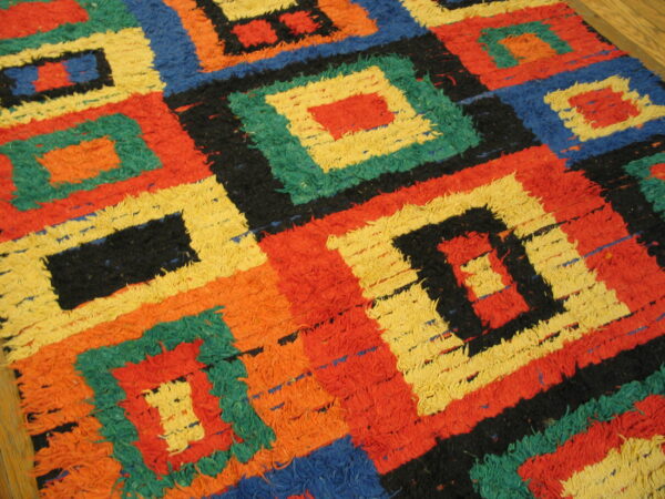 High-pile rug with nested geometric squares in red, yellow, blue, green, black, and orange on wood flooring.