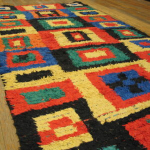 Multi-colored shaggy rug featuring concentric square patterns in red, yellow, blue, and black on wood floor.