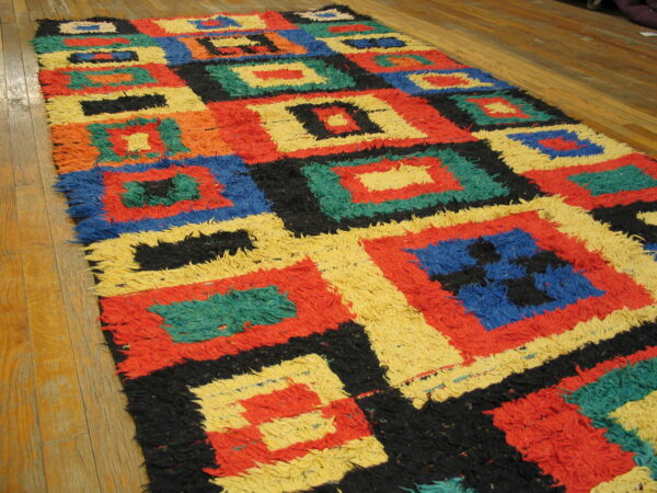 Multi-colored shaggy rug featuring concentric square patterns in red, yellow, blue, and black on wood floor.