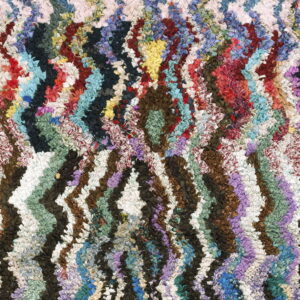 Shaggy multicolored rug with dense texture and complex chevron and diamond geometric designs.