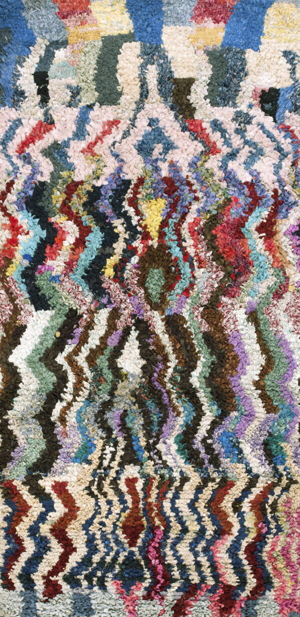 Shaggy multicolored rug with dense texture and complex chevron and diamond geometric designs.