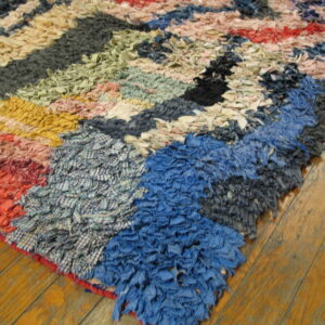 Multicolor rag rug with chunky texture and geometric patterns is displayed on rustic wood flooring.