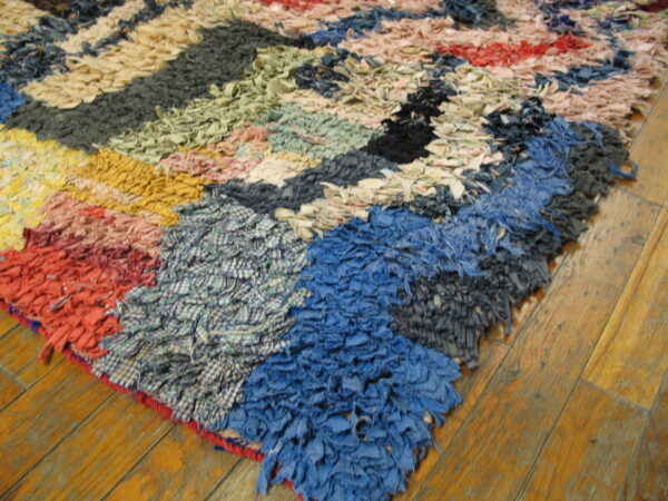 Multicolor rag rug with chunky texture and geometric patterns is displayed on rustic wood flooring.