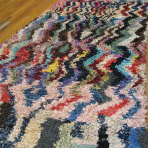 Shaggy runner rug with a multicolor zig-zag pattern made of fabric strips on hardwood flooring.