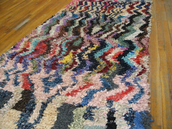 Shaggy runner rug with a multicolor zig-zag pattern made of fabric strips on hardwood flooring.