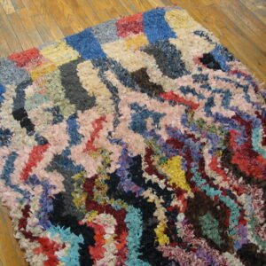 Abstract, shaggy rag rug in bright mixed colors, including blue, pink, and yellow, rests on wood flooring.