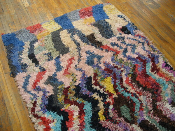 Abstract, shaggy rag rug in bright mixed colors, including blue, pink, and yellow, rests on wood flooring.
