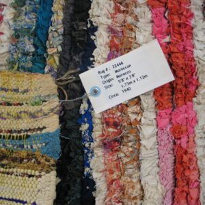 Multicolor rag rug featuring pink, blue, orange, and white striped sections and a visible attached product tag.