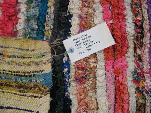 Multicolor rag rug featuring pink, blue, orange, and white striped sections and a visible attached product tag.