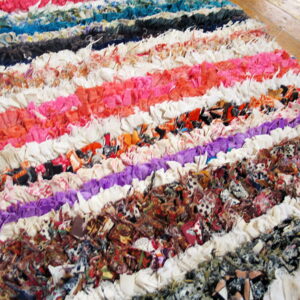A multicolored, shaggy rag rug with bright horizontal stripes rests on light brown hardwood flooring.