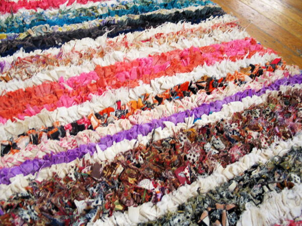 A multicolored, shaggy rag rug with bright horizontal stripes rests on light brown hardwood flooring.