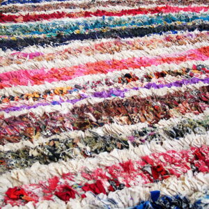 Close-up view of a colorful, high-texture striped rag rug resting on brown wooden plank flooring.
