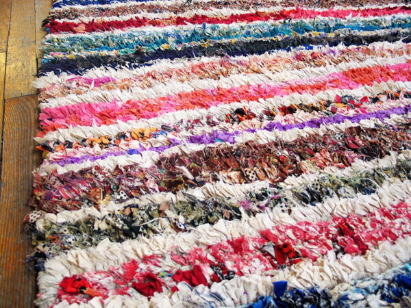 Close-up view of a colorful, high-texture striped rag rug resting on brown wooden plank flooring.