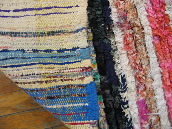 Textured detail of a low-pile striped woven rug beside a high-pile shaggy rug in blue, white, and pink tones.