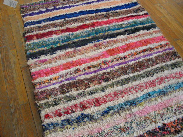 Multicolor striped rag rug with chunky texture lying on light brown wooden floorboards.