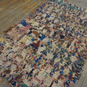 Colorful high-pile rag rug with a cream grid pattern lying on distressed light brown wood planks.
