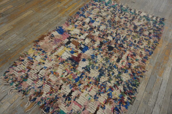 Colorful high-pile rag rug with a cream grid pattern lying on distressed light brown wood planks.