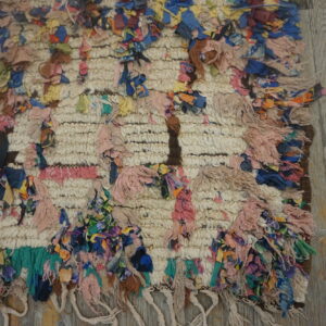 High-pile, textured cream rug with colorful knotted fabric strips lying on weathered gray wood floor.