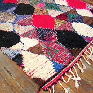 A multicolored shag rag rug featuring large irregular blocks rests on rustic wooden flooring.