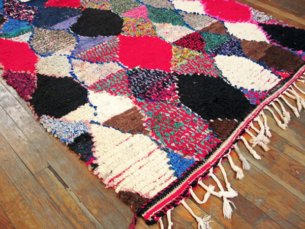 A multicolored shag rag rug featuring large irregular blocks rests on rustic wooden flooring.