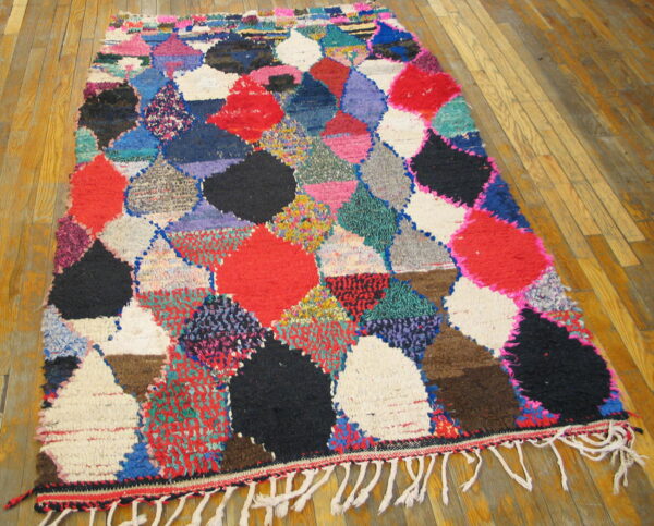 Vibrant high-pile rug with abstract red, black, pink, and blue patchwork diamonds on a wood floor.