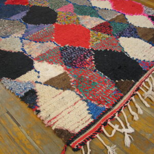Textured multicolor patchwork rug with large shaggy shapes and knotted fringe on a wood floor.